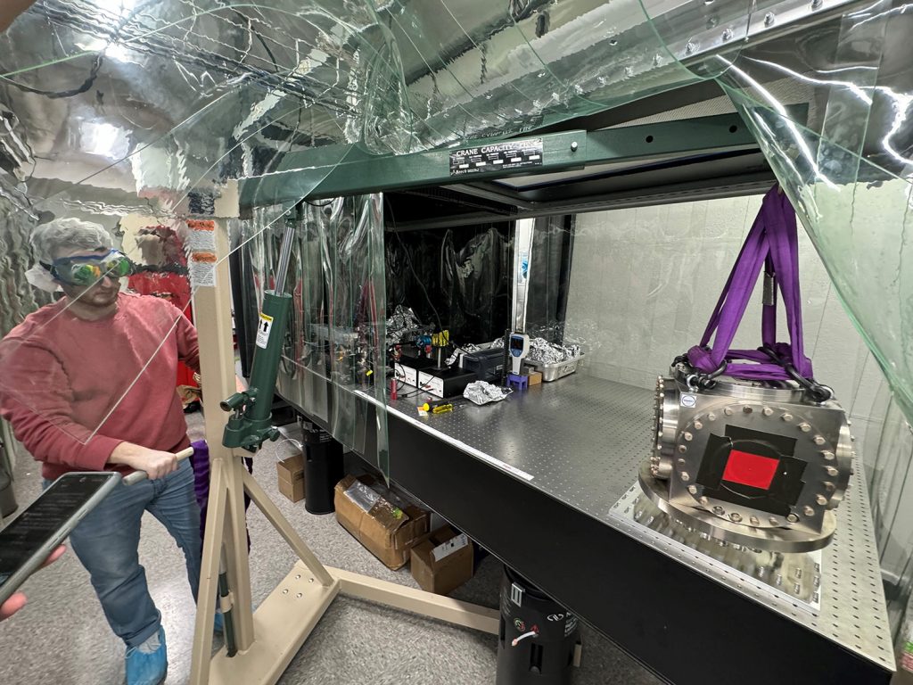 Ian MacMillan using an engine hoist to lift a vacuum chamber onto the table to be used for the laser filter cavity. Photo: Daniel Grass, Caltech